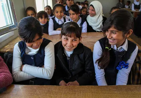Three girls sit at a desk in a caravan that serves as a temporary classroom at Salsabil Primary School for Girls in Fallujah. © UNICEF Iraq/2016/Khuzaie