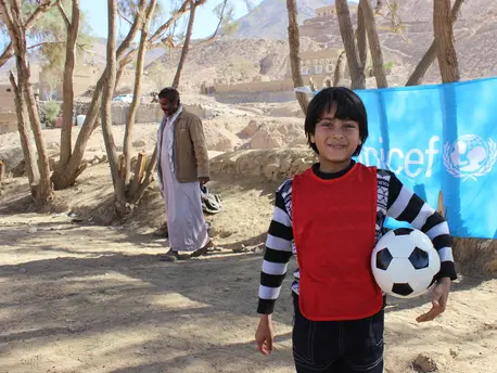On 3 March 2016 in Yemen, a child holds a football in front of a UNICEF flag in Sa’ada. Here, psychosocial support is provided to children in a UNICEF child-friendly space. unicef, unicef usa, yemen, soccer, football, refugee children