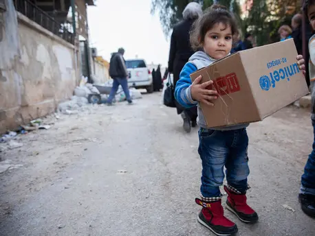 A child carries a box of winter clothes from UNICEF in Al-Waer, a neighborhood in Homs. UNICEF, Syria, humanitarian aid