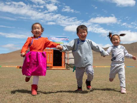 In June 2018 in Mongolia, three preschool-age children run hand-in-hand outside their mobile 'ger' kindergarten in the Janjin bagh area in Bayankhongor Province. 