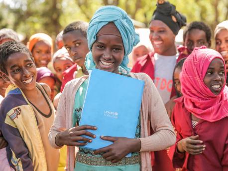 Surrounded by her classmates, a girl holds her UNICEF notebook at Shawe Primary School, Harana Buluk Woreda, in Ethiopia's Oromia Region in 2019.