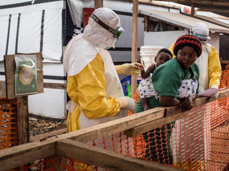 A health worker wearing a gown, gloves and goggles checks a child potentially infected with Ebola being carried on the back of a caregiver at the Ebola Treatment Center of Beni, North Kivu province, Democratic Republic of Congo on March 24, 2019.