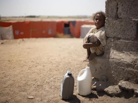 A child from Yemen's Al-Meshqafah camp takes a break while carrying heavy jugs of drinking water from the supply tanks to the camp in February 2019.
