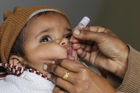 A health worker vaccinates 1-year-old Ahmad at the door of his family's home during a 2019 national immunization campaign in Pakistan. 