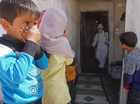Syrian children watch a member of the Syrian Civil Defence, known as the White Helmets, disinfecting a former school building currently inhabited by displaced families in the town of Binnish in northwestern Idlib Governorate, Syria, on March 26, 2020. Syrian children watch a member of the Syrian Civil Defence, known as the White Helmets, disinfecting a former school building currently inhabited by displaced families in the town of Binnish in northwestern Idlib Governorate, Syria, on March 26, 2020.