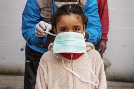 On 31 March 2020, seven-year-old Francesca [NAME CHANGED] is given a protective mask by INTERSOS/UNICEF outreach worker Abdoul Bassite, prior to a health screening in the informal settlement in Rome, Italy, where she lives.
