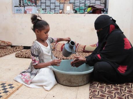 On 4 April 2020, Fatima pours water to help her mother wash her hands thoroughly, in a centre for internally displaced persons in Aden, Yemen. 
