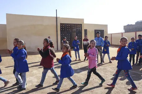 14 children smiling and playing outside in a sunny enclosed area.