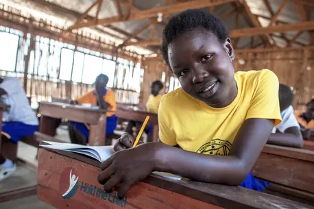 African child sitting at a desk in school with a book open. Smiling and looking at the camera