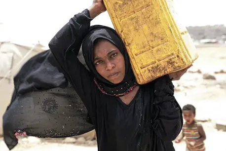 Ashwaq, 14, whose family was displaced from Saada, Yemen, carries water in the Khamir settlement in Amran. Ashwaq, 14, whose family was displaced from Saada, Yemen, carries water in the Khamir settlement in Amran.