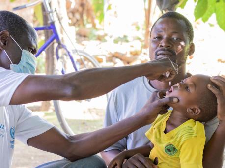 A father holds his 2-year-old son while he receives his polio vaccine in Masulama village, Karonga District, northern Malawi. 