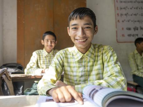 Child smiles while sitting at his desk in middle school in India