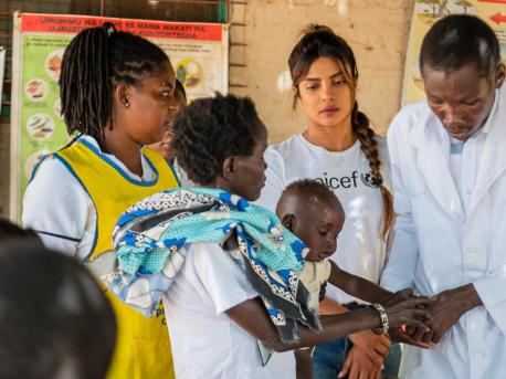 Brenda Ekiru holds her 10-month-old son, Kevin, as he gets a medical check-up from a health officer while UNICEF Goodwill Ambassador Priyanka Chopra Jonas, center, looks on.