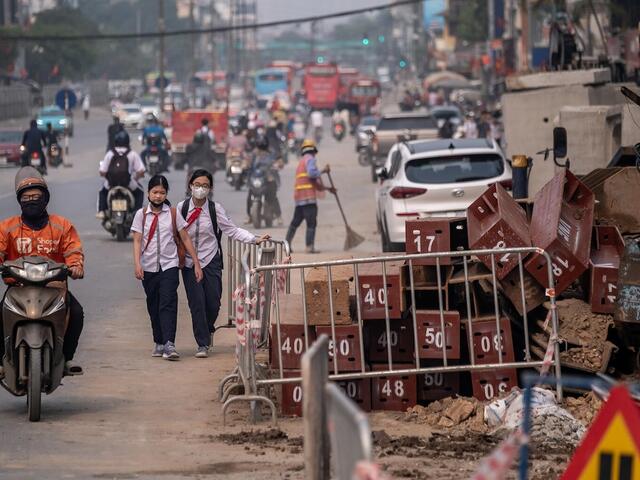 People wearing masks navigate through a dusty construction area on Kim Dong Street, Hai Ba Trung District, Hanoi, Vietnam.