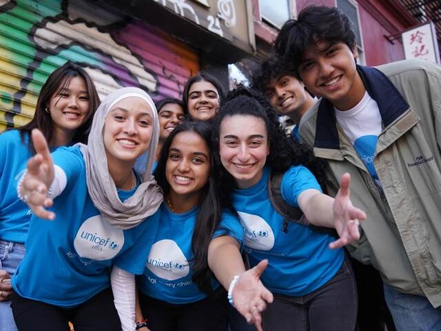 A group of smiling UNICEF club members wearing UNICEF T shirts stand in front of a mural. 