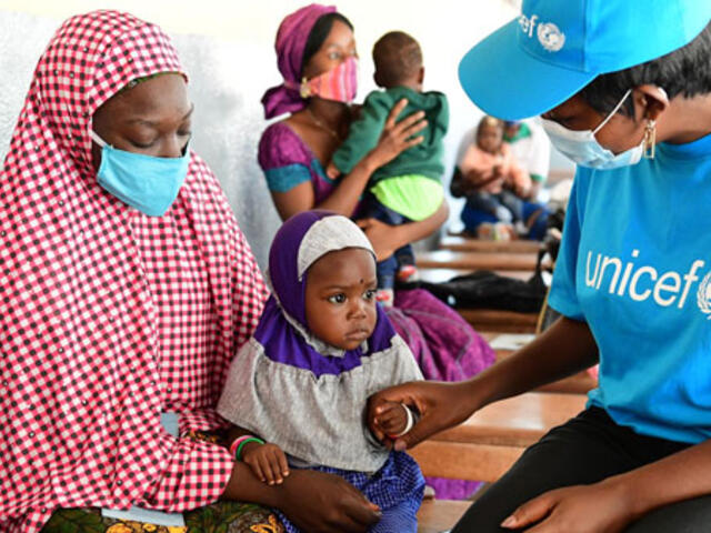 UNICEF worker sitting with a mother and child.