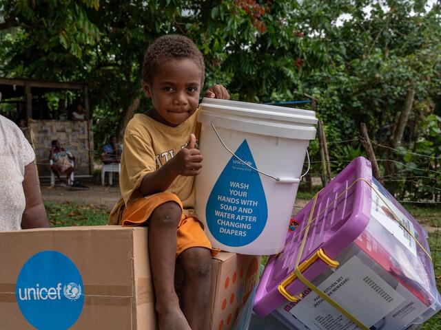 Four-year-old Johnathan sits holding items included in an emergency kit distributed by UNICEF and partners to earthquake-affected families in Erakor Bridge Community in south Efate, Vanuatu, in December 2024.