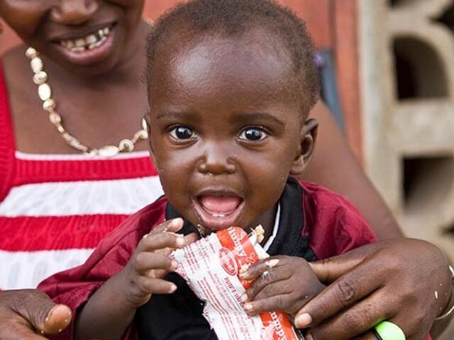 Young boy being held by his mother eating a RUTF packet