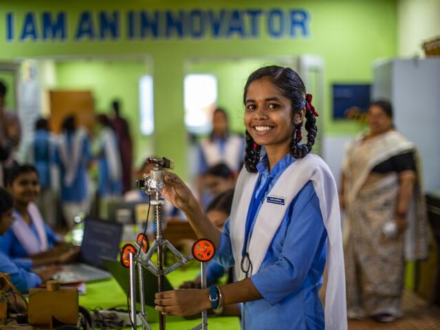 Smiling girl in blue shirt standing in front of table 