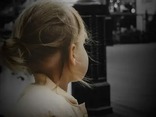 A young girl, around age 3, shown from behind, looks off into the distance
