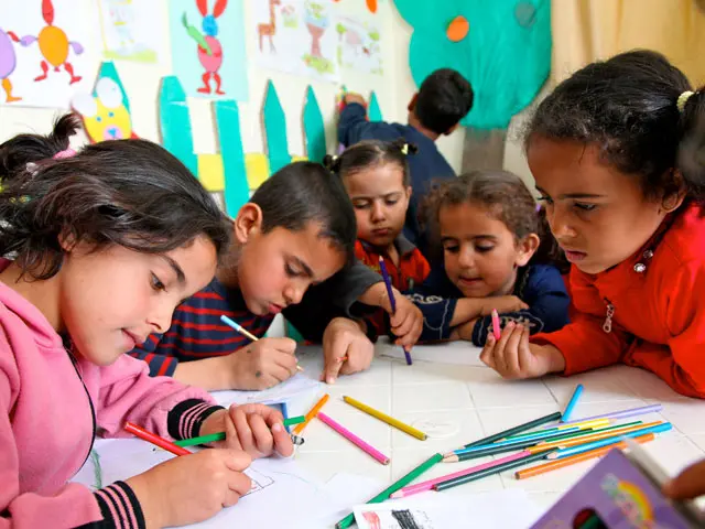 Children gathered around a table, coloring on a big sheet of paper