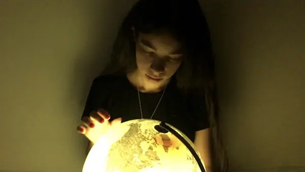 A young girl looks at a glowing globe in a darkened room