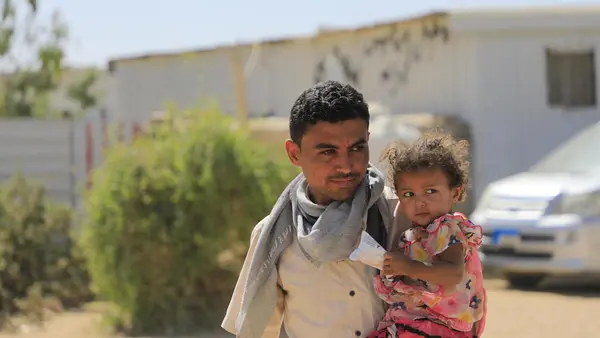 In 2022, a father holds his 2-year-old daughter outside the family's home in a camp for internally displaced families in Yemen's Marib governorate. 