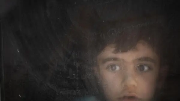 child peering out a window in a darkened room