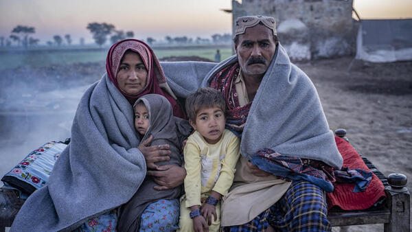 A family sits on a charpoy outside their house after receiving UNICEF’s winter kit in Zangi Brohi Village, Dadu District, Sindh.