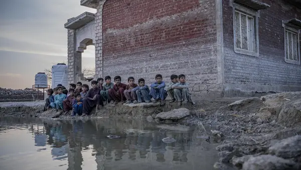 Children sit beside a lake of contaminated floodwater near Zangi Brohi Village, Dadu District, Sindh