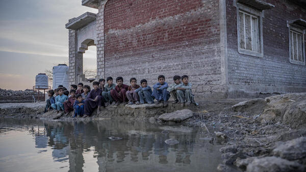 Children sit beside a lake of contaminated floodwater near Zangi Brohi Village, Dadu District, Sindh
