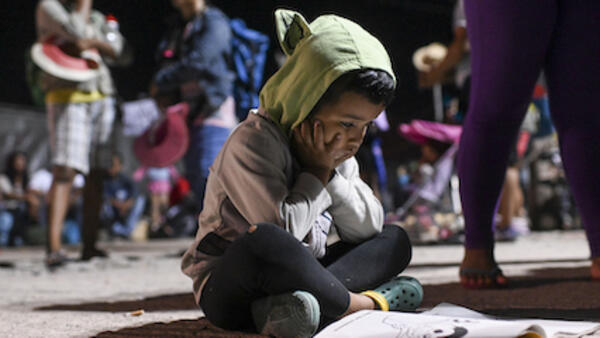 A child migrant sits on the floor with a coloring book.