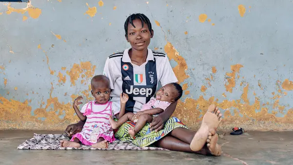  A young mother sits with her 2-month-old son and 22-month-old daughter Marie, who is being treated for severe acute malnutrition, outside their room at the UNICEF-supported nutrition center at Saint Jean de Dieu Hospital, Tanguiéta, northern Benin.