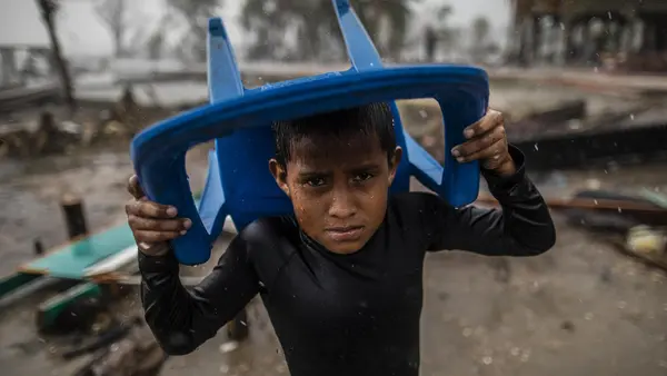 In Bilwi, Nicaragua, a young boy holds a plastic chair over his head to shield himself from pelting rain while standing in the spot where his house used to stand until it was destroyed by Hurricane Iota.