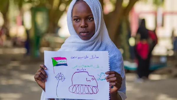 A young girl shows a drawing of a tank representing her experiences with conflict in Sudan at a UNICEF-supported Child-Friendly Space in Madani.