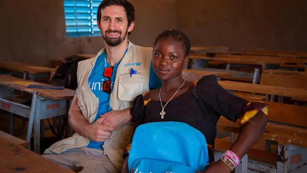 In October 2023, UNICEF staff Benoit Sicard sits with 14-year old Juliette in a classroom in Kaya, Centre Nord region, Burkina Faso.