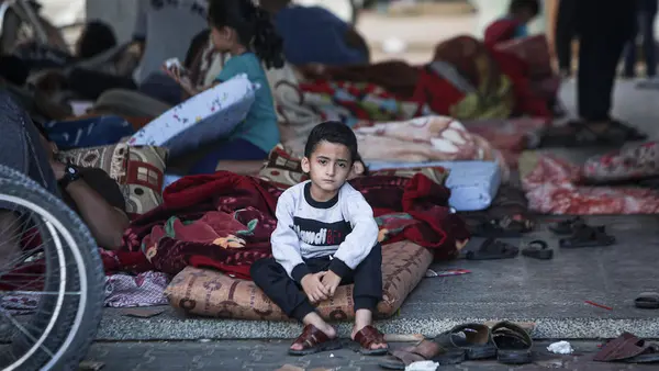 Ahmad, 5, sits on his mattress in a shelter courtyard in Gaza, surrounded by hundreds of other displaced people. 