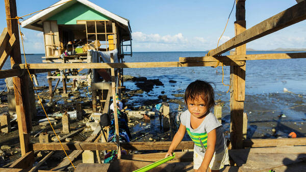 Two-year-old Gwendolyn in Barangay Fatima, Purok 1 in Ubay, Bohol, Philippines, stands among the ruins of her family's home, which was destroyed by a typhoon.