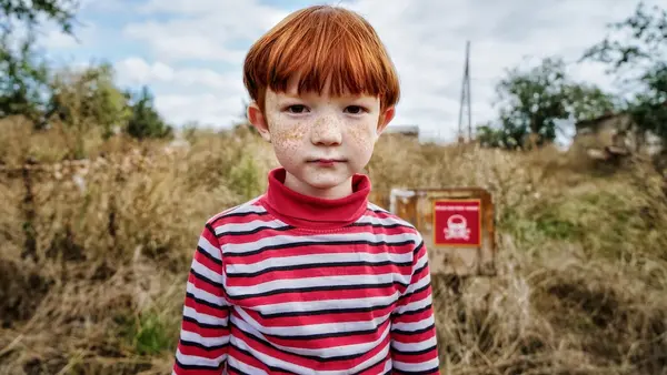 Leonid, 6, stands in front of a sign that reads "Danger of Mines" in the Kharkiv region of Ukraine.