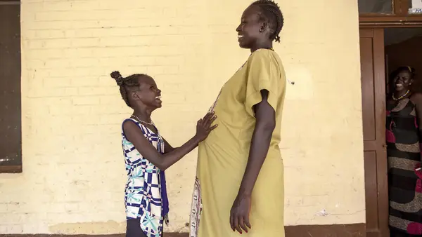 Eleven-year old Nyanyiik rests her hands on the stomach of Sundoay John - who is 9 months pregnant with her second child - outside the UNICEF-supported maternity ward at Malakal Teaching Hospital, South Sudan.