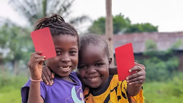 In Kwango Province, Democratic Republic of the Congo (DRC), 5-year-olds Makiese, left, and Madinu brandish red cards after receiving their polio vaccinations in 2023.