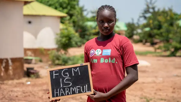 A girl in The Gambia holds a sign protesting against female genital mutilation.