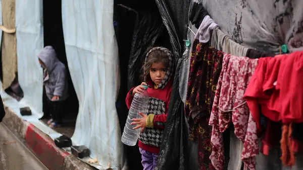 A little girl stands in front of her family's tent , holding an empty water bottle in the city of Rafah, southern Gaza Strip.