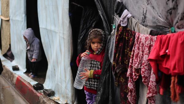 A little girl stands in front of her family's tent , holding an empty water bottle in the city of Rafah, southern Gaza Strip.