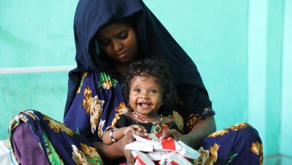 A mother holds her smiling daughter as she receives Ready-to-Use Therapeutic Food (RUTF) from a UNICEF-supported health worker in Ethiopia.