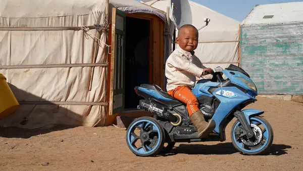 Ochir-erdene, 3, riding on his toy motorcycle in front of his herder family's ger home in a remote part of Dundgobi, Mongolia.