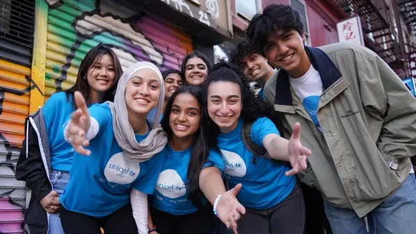 A group of smiling UNICEF club members wearing UNICEF T shirts stand in front of a mural. 