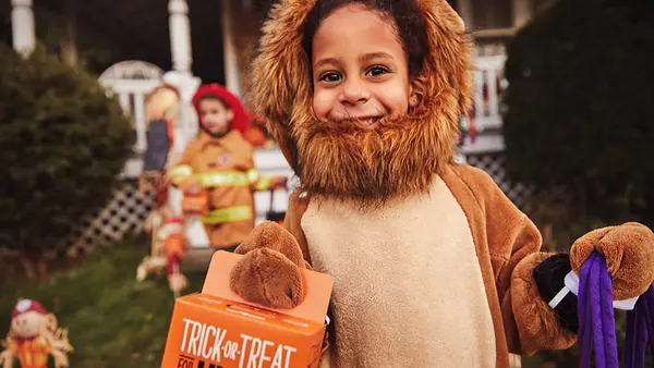Kid in lion costume holding little orange box trick-or-treating for UNICEF.