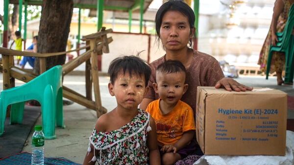 On March 31, 2025, a woman with two small children poses for a photograph with a box of UNICEF hygiene kits distributed to earthquake survivors in the Sagaing region of Myanmar. 