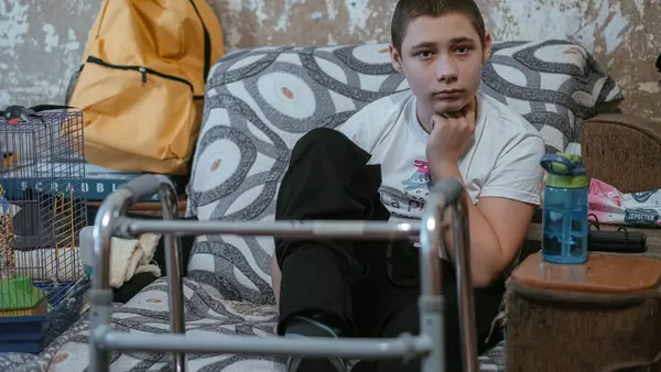 In Nikopol, Kharkiv oblast, eastern Ukraine, Nazar, 13, sits in his family's living room, his walker nearby. His legs and feet were injured by an explosive remnant of war. 